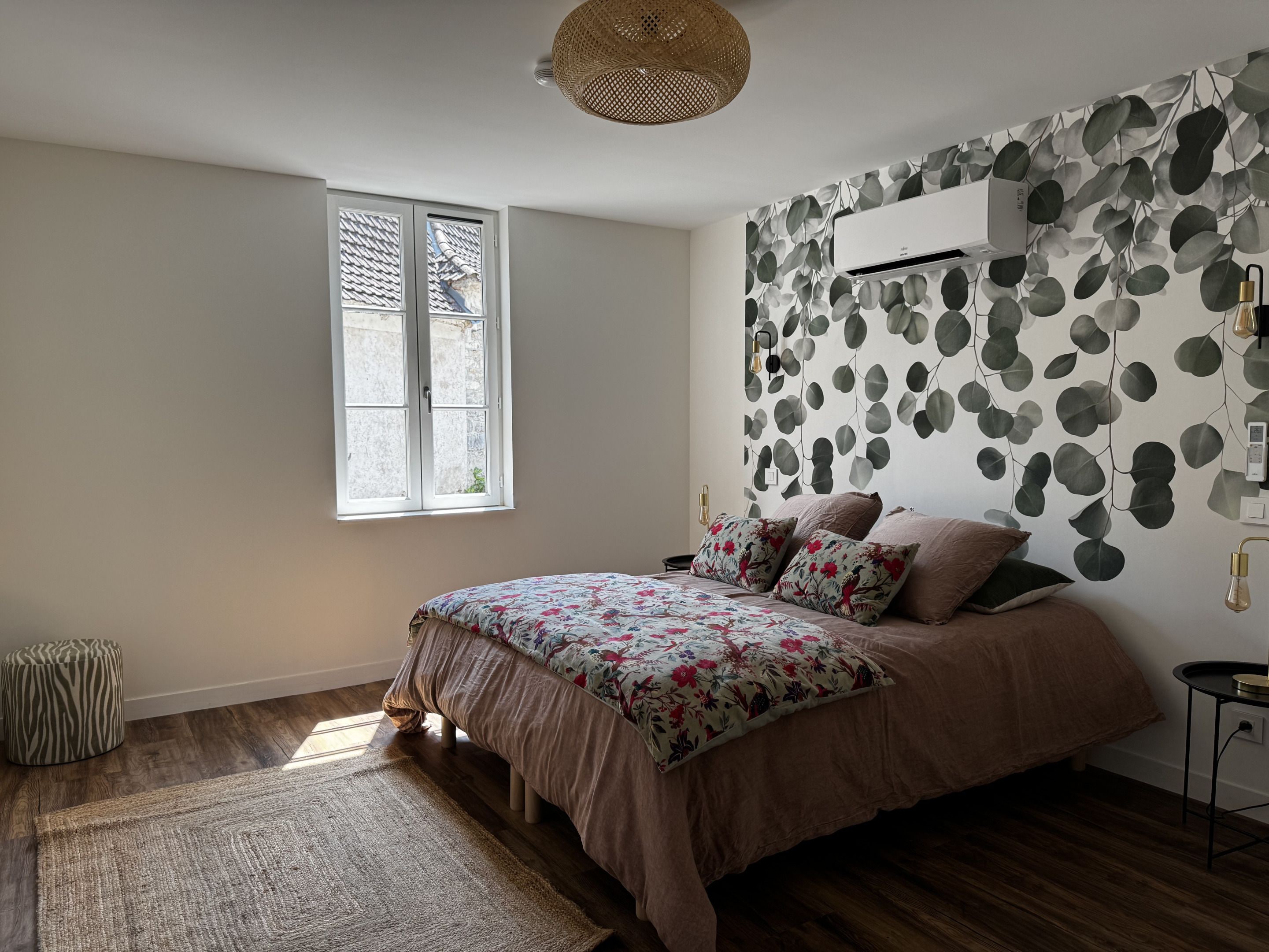 Un dormitorio con cama, ventana, aire acondicionado de pared y pared con diseño.