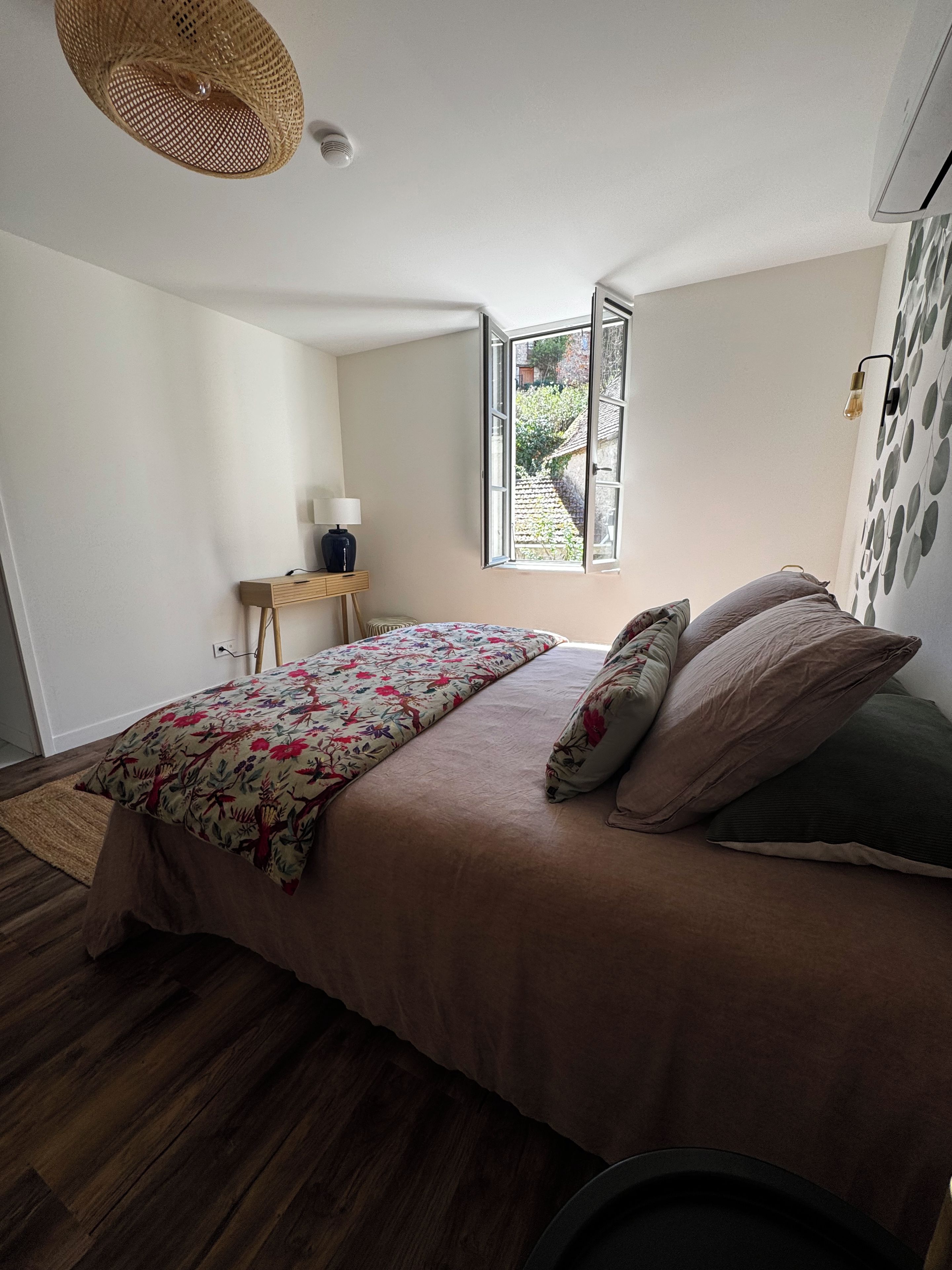 Un dormitorio con una cama, una mesita de noche, una lámpara, un ventanal y una pared con un diseño circular.