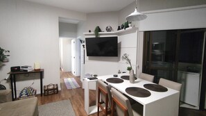 A modern kitchen with a white countertop, bar stools, a flat-screen TV mounted above the counter, and a dining area with a table and chairs. - Modern and Cozy Apartment 200 Meters from Praia Ingleses in Florianópolis (Florianópolis)