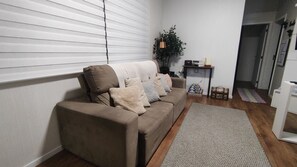 A living room with a beige sofa, a patterned rug, a small table with books, and a potted plant. - Modern and Cozy Apartment 200 Meters from Praia Ingleses in Florianópolis (Florianópolis)