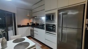 A modern kitchen with stainless steel appliances, a dining table with placemats, and a window with a view. - Modern and Cozy Apartment 200 Meters from Praia Ingleses in Florianópolis (Florianópolis)