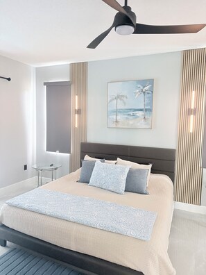 Een moderne slaapkamer met een bed, een plafondventilator, een wanddecoratie en een klein tafeltje.