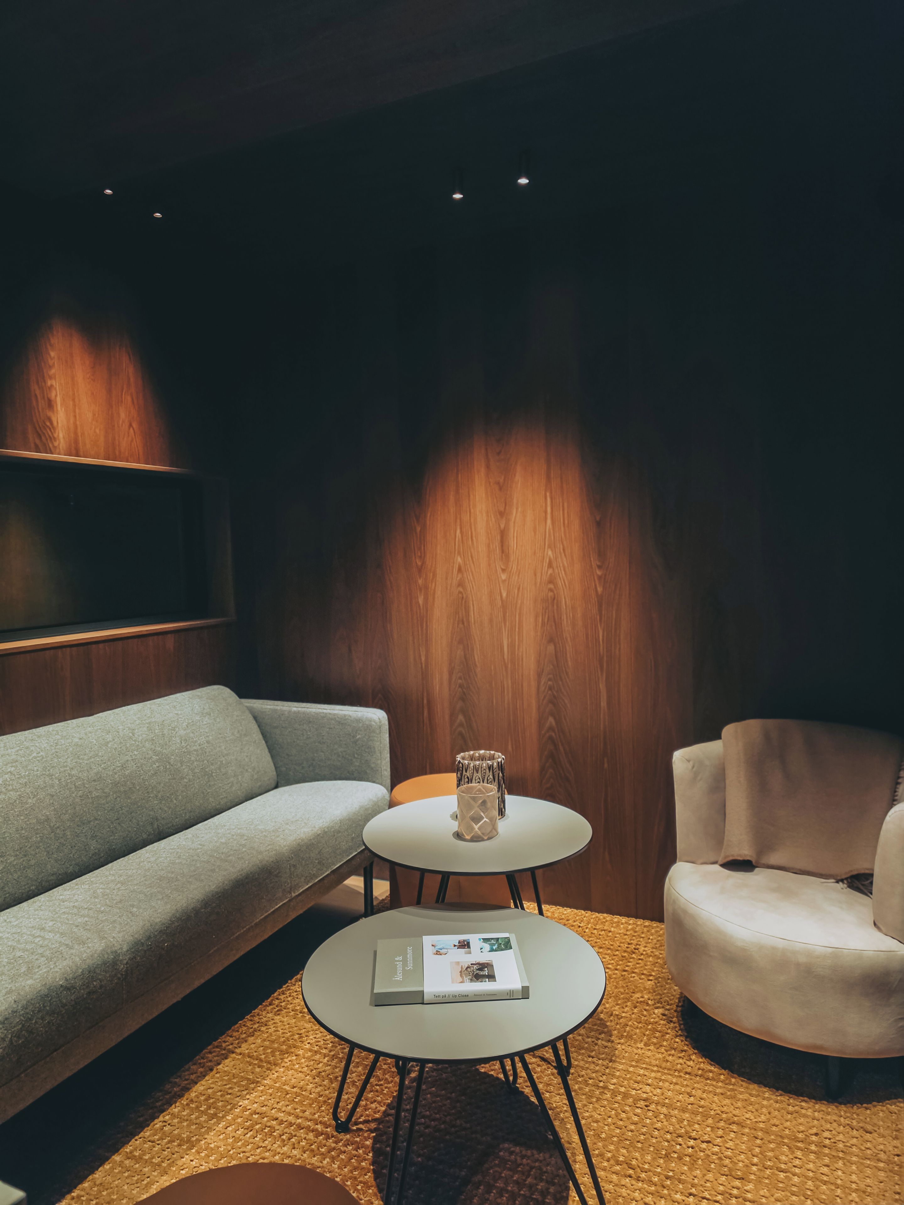 Un saló modern amb un sofà gris, una taula de centre rodona amb una revista, una taula petita rodona amb un objecte decoratiu, i un butac armchair beix.