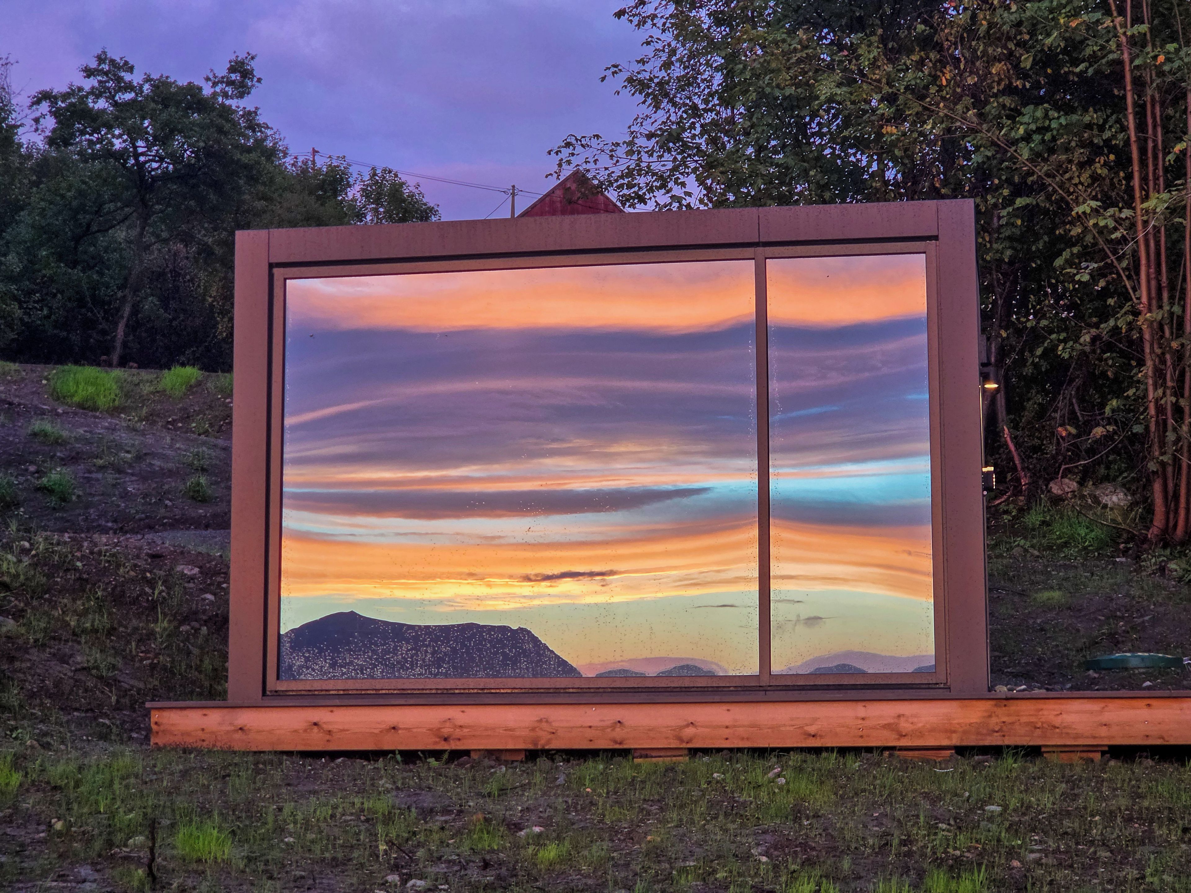 Ein großes Fenster mit Blick auf einen Sonnenuntergang über einer Berglandschaft.
