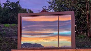 Ein großes Fenster mit Blick auf einen Sonnenuntergang über einer Berglandschaft.
