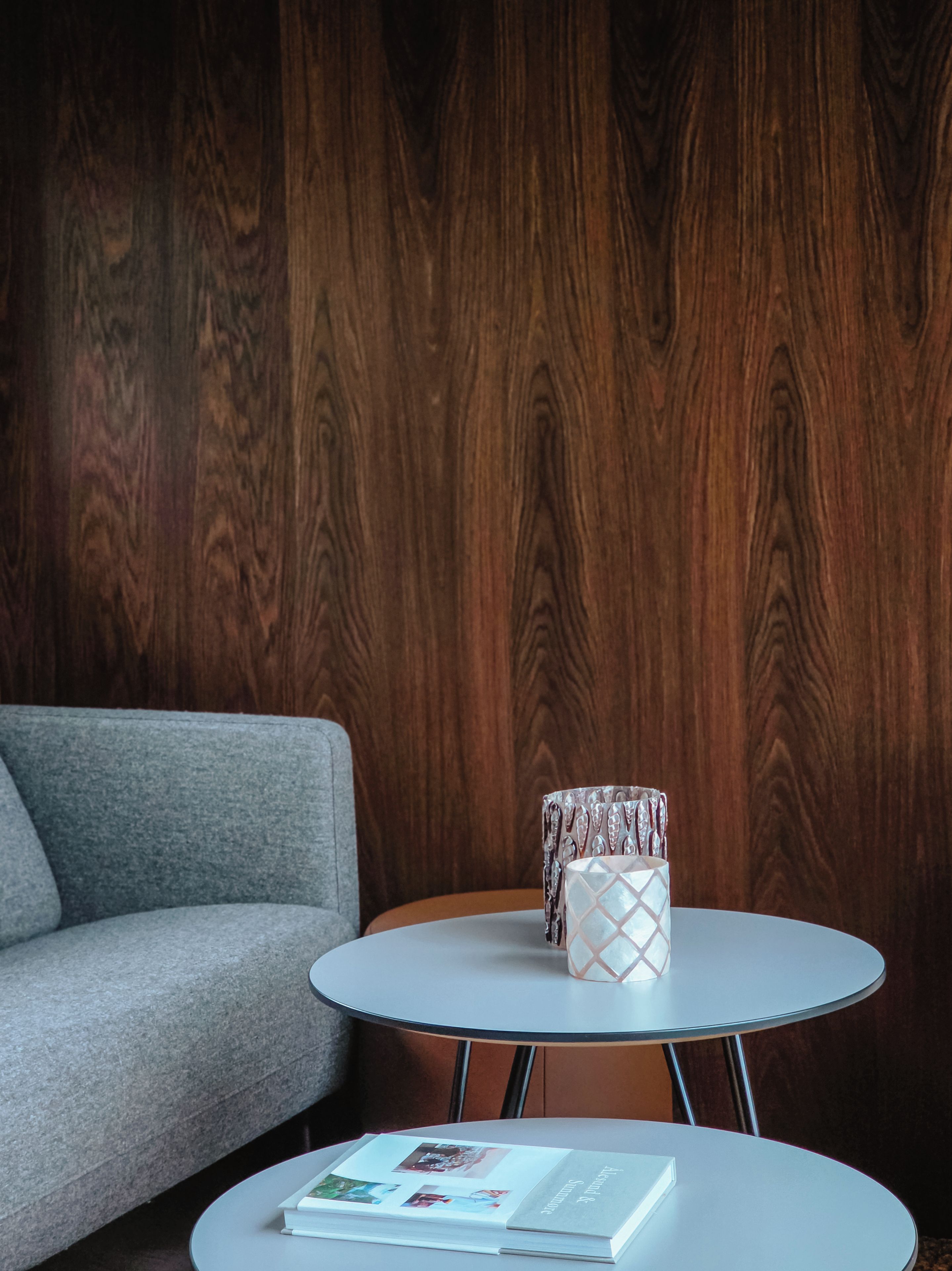 Een kamer met een grijze bank, een ronde tafel met een boek, en een geborduurde plaid op de tafel.