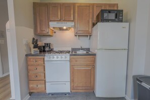 A compact kitchen with wooden cabinets, a white stove, a sink, and a refrigerator. - Sunlit Bow Window Studio | Back Bay (Boston)