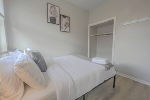 A bedroom with a bed, pillows, a bedside table, a wardrobe, and two framed pictures on the wall. - Sunlit Bow Window Studio | Back Bay (Boston)
