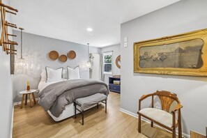 Een slaapkamer met een bed, nachtkastjes, een stoel, een kroonluchter en een ingelijste foto aan de muur.