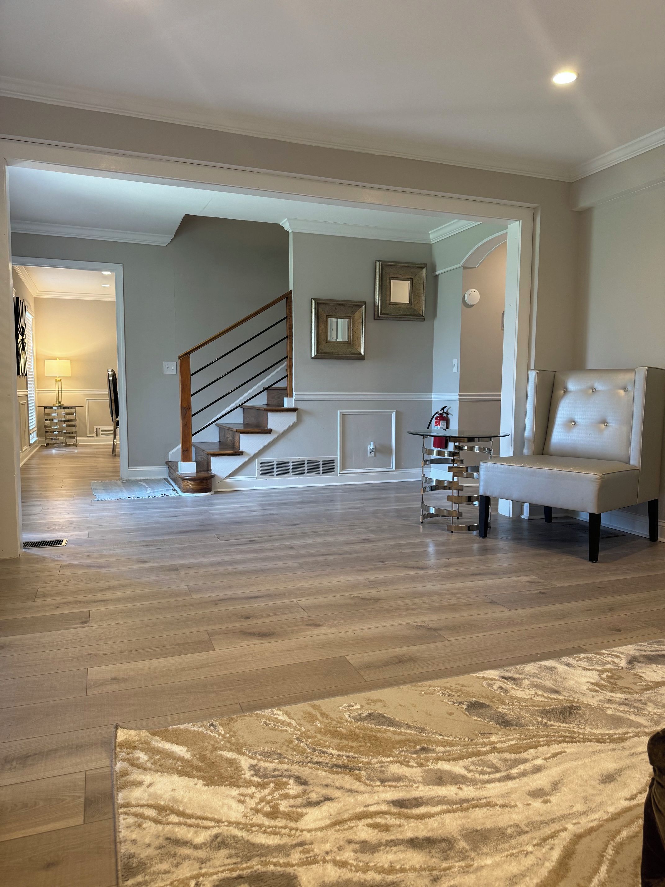 A spacious living room with hardwood flooring, a staircase, and a leather armchair.