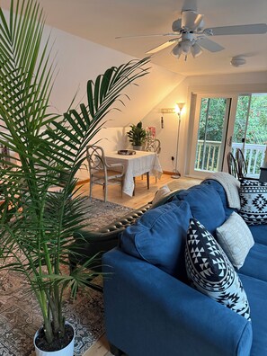 A living room with a blue sofa, patterned cushions, a potted plant, and a dining area with a table and chairs. - Serene 3-bedroom 3-full BR house with Heat in charming Manchester Center, VT. (Manchester)