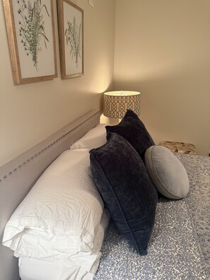 A bed with a patterned bedspread, two pillows, a bedside lamp, and two framed botanical prints on the wall. - Serene 3-bedroom 3-full BR house with Heat in charming Manchester Center, VT. (Manchester)