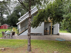 Une maison à deux étages avec un porche couvert, une table à manger avec des chaises et un petit jardin.