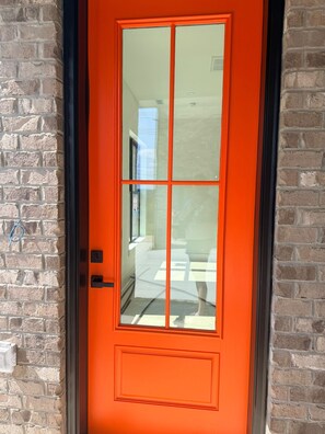 A bright orange door with a glass panel, set in a brick wall. - NEW Walk Neyland Modern Vol - 3 king suites, rooftop deck w Hottub (Knoxville)