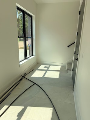 Ein Zimmer mit einem großen Fenster, einer Tür und einem sichtbaren Stromrohr am Boden.
