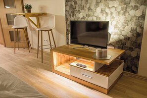 A modern living room with a wooden TV stand, a flat-screen TV, and a small white cabinet. - Hexagon Apartment Budapest (Budapest)