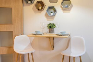 A dining area with a wooden table, two white chairs, a potted plant, and hexagonal shelves on the wall. - Hexagon Apartment Budapest (Budapest)