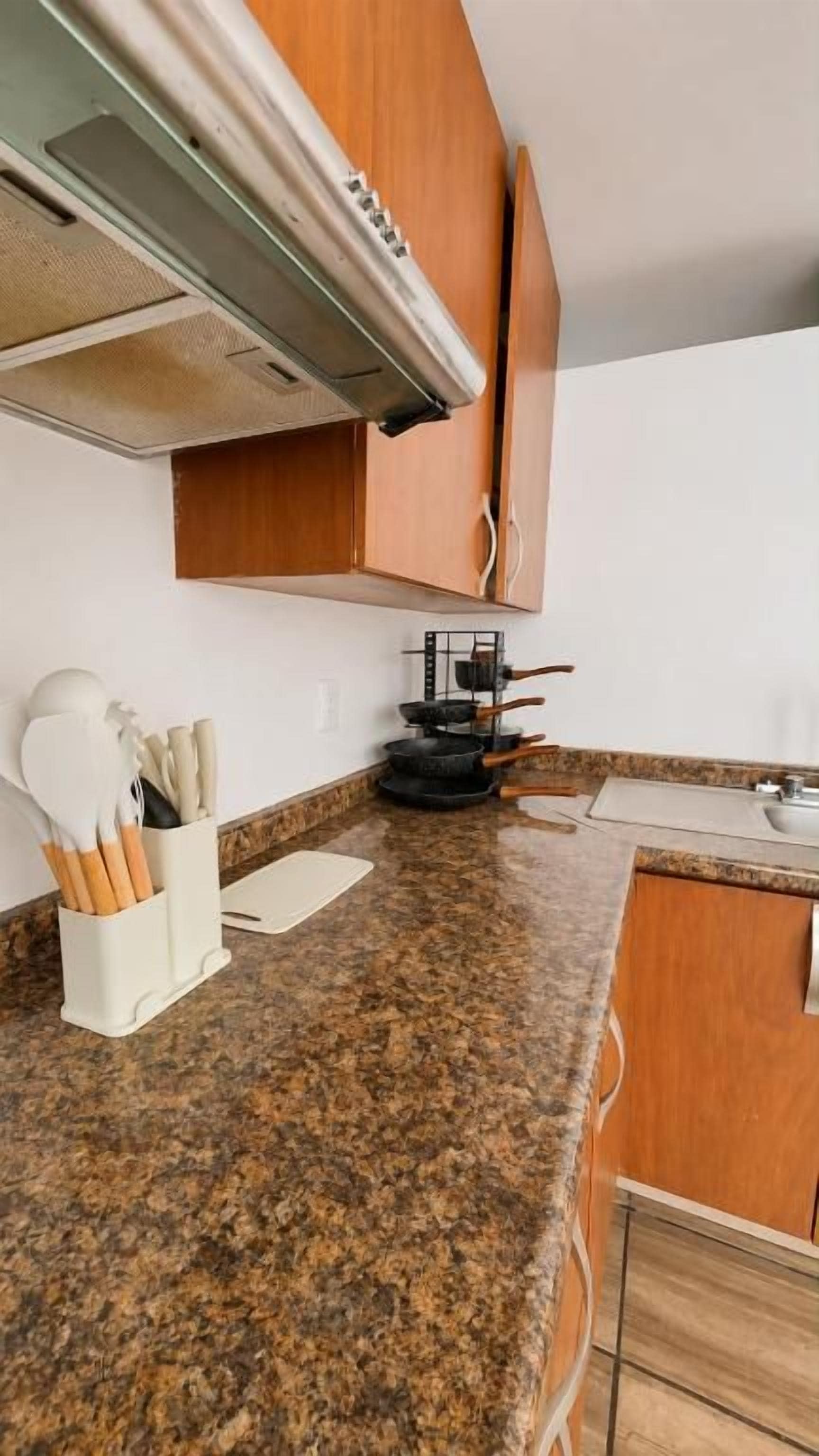 A kitchen with granite countertops, wooden cabinets, and a stainless steel range hood.