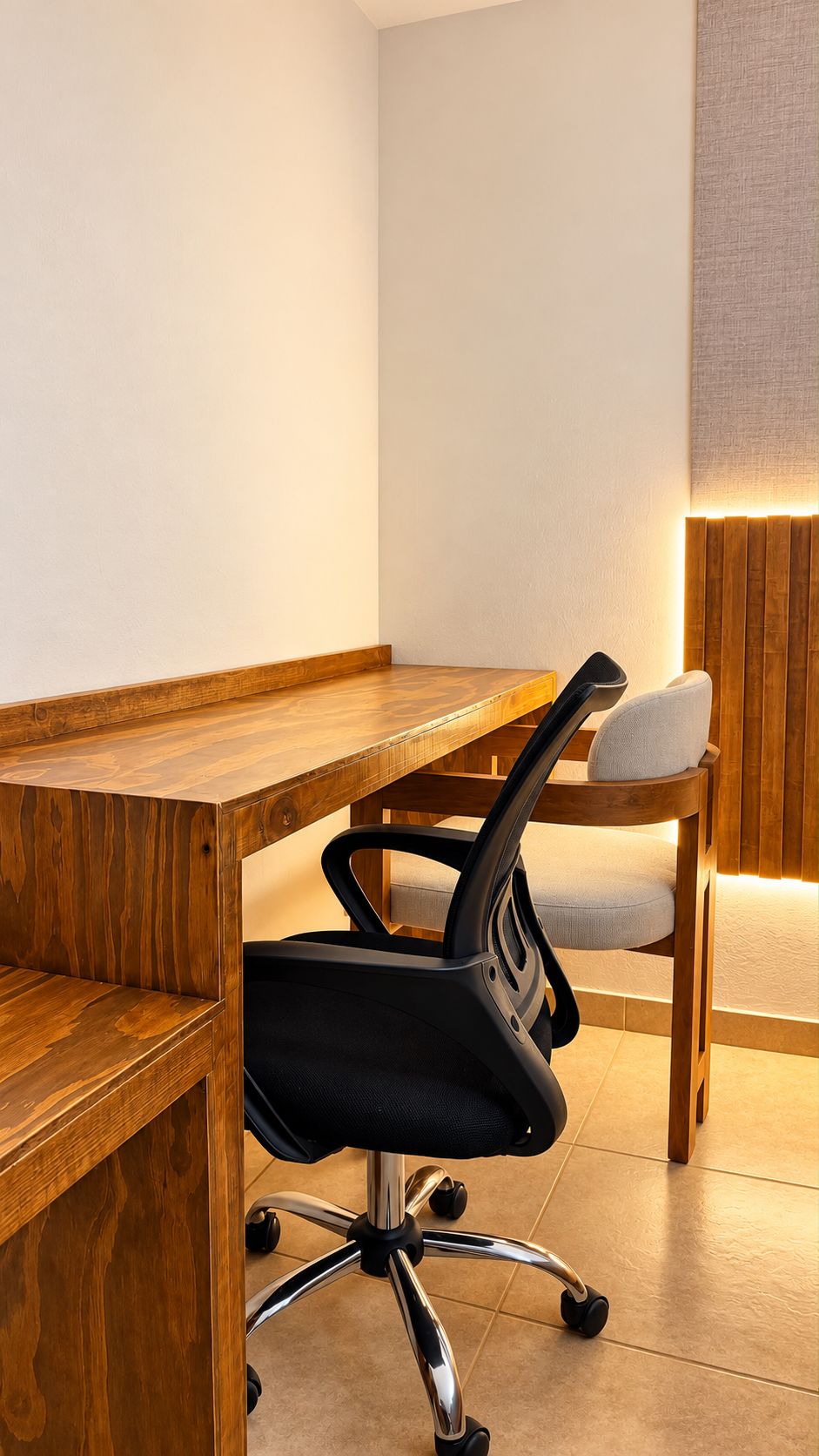 Un escritorio de madera con una silla de oficina negra, un banco acolchado y una lámpara fijada a la pared.