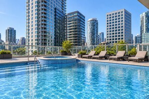 Ein Pool auf dem Dach mit Liegestühlen und einer Whirlpool-Anlage, umgeben von hohen Gebäuden.