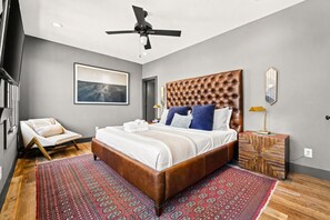 A modern bedroom with a large bed, a ceiling fan, a chair, and a nightstand. - Rooftop skyline views, walkable WeHo house, sleeps 10 near Geodis Park (Nashville)