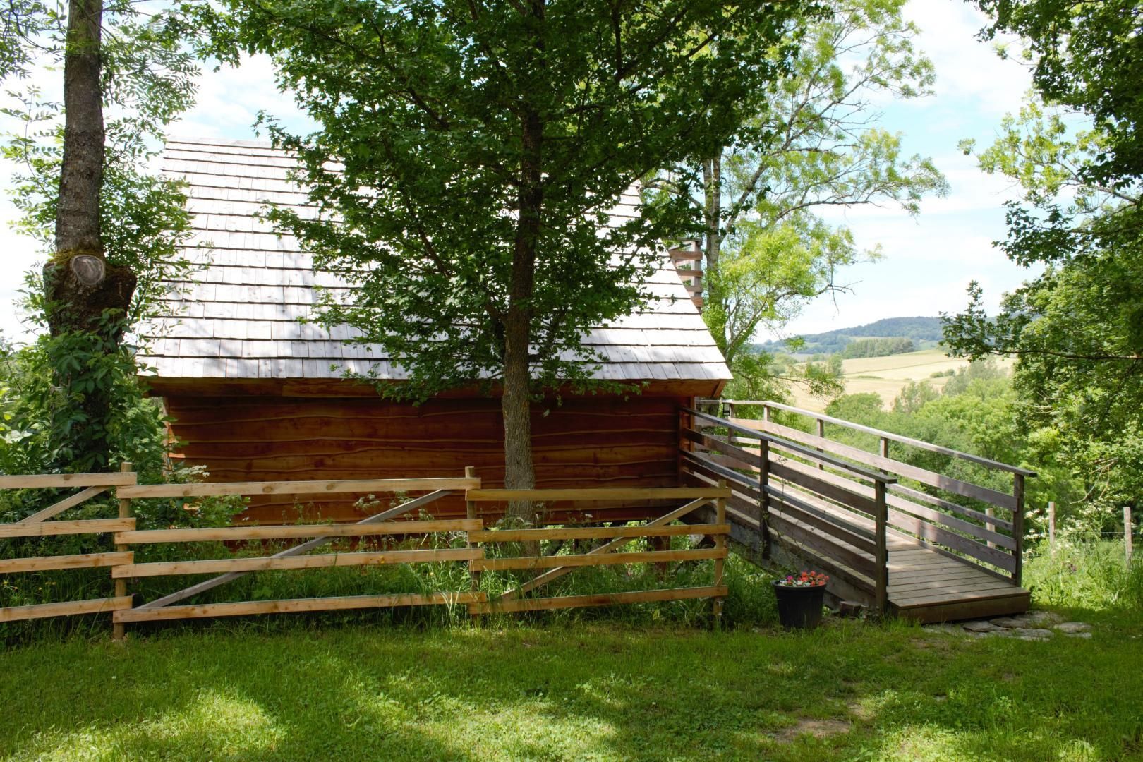 A wooden cabin with a metal roof, surrounded by a wooden fence and a small wooden bridge leading to it.