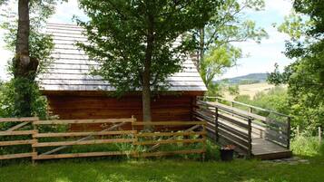 A wooden cabin with a metal roof, surrounded by a wooden fence and a small wooden bridge leading to it.