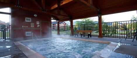 A hot tub under a wooden pavilion with a bench and a fence.