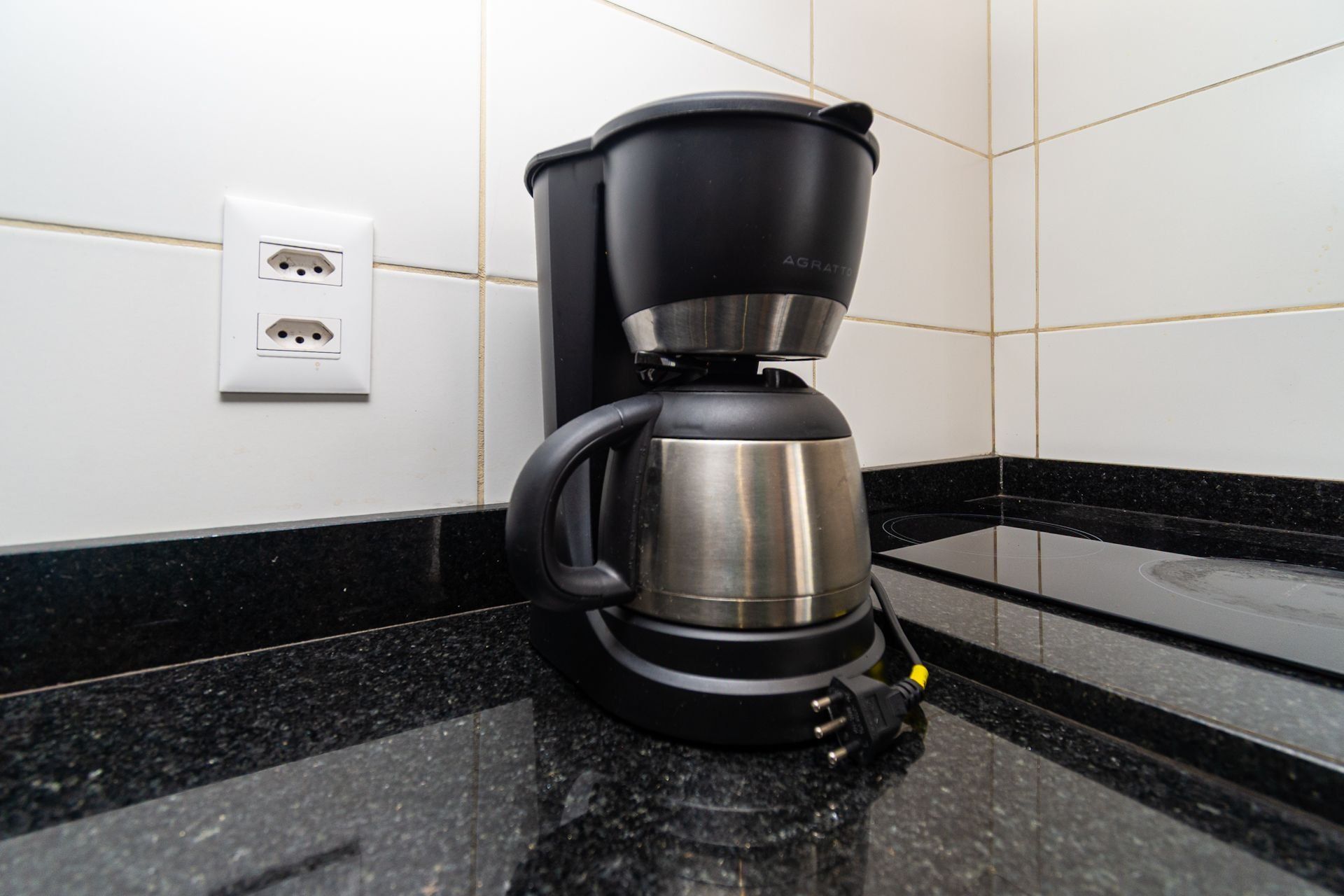 Eine Kaffeemaschine auf einer Küchenarbeitsplatte mit schwarzer Arbeitsfläche und weiß gefliestem Spritzschutz.