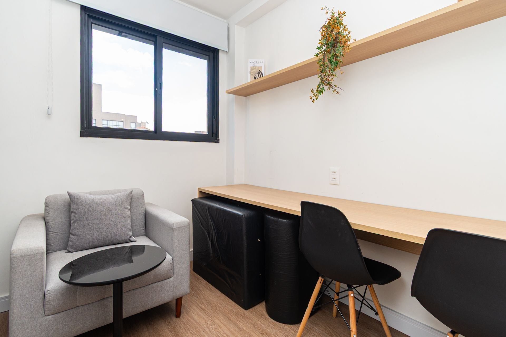 A modern living space with a sofa, a small round table, a wooden desk, and two black chairs.