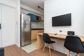 A compact kitchen with a refrigerator, microwave, and a flat-screen TV mounted on the wall. - Bracon Perdizes by Housi (São Paulo)