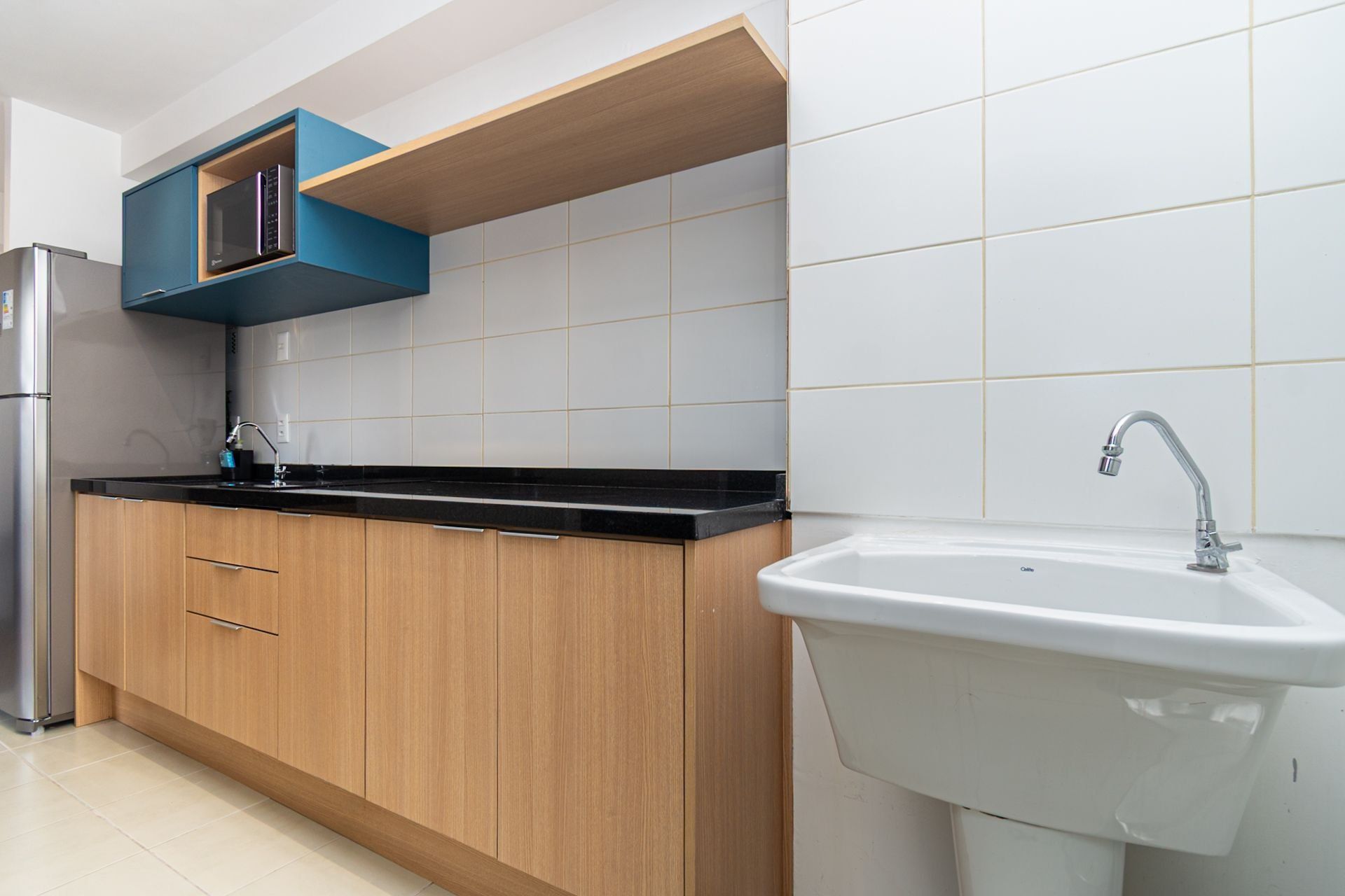 A modern kitchen with wooden cabinets, a black countertop, a stainless steel refrigerator, a built-in microwave, and a white sink with a faucet.