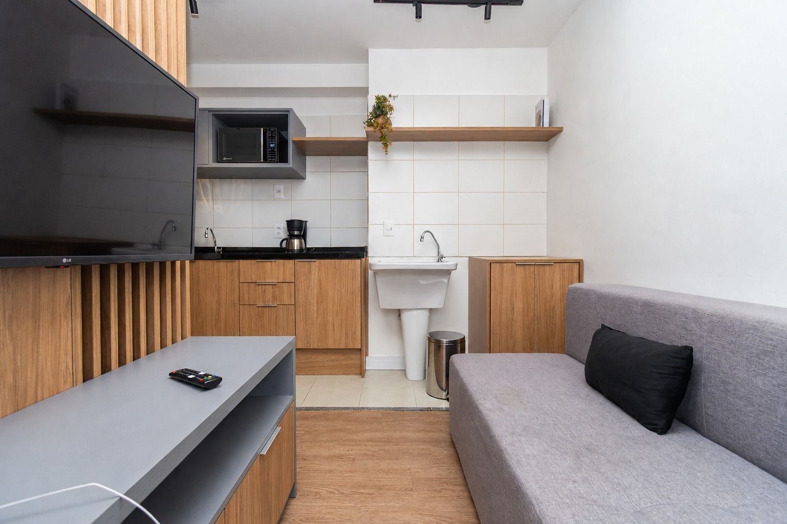 Een kleine keuken met een magnetron, spoelbak en houten kastjes.