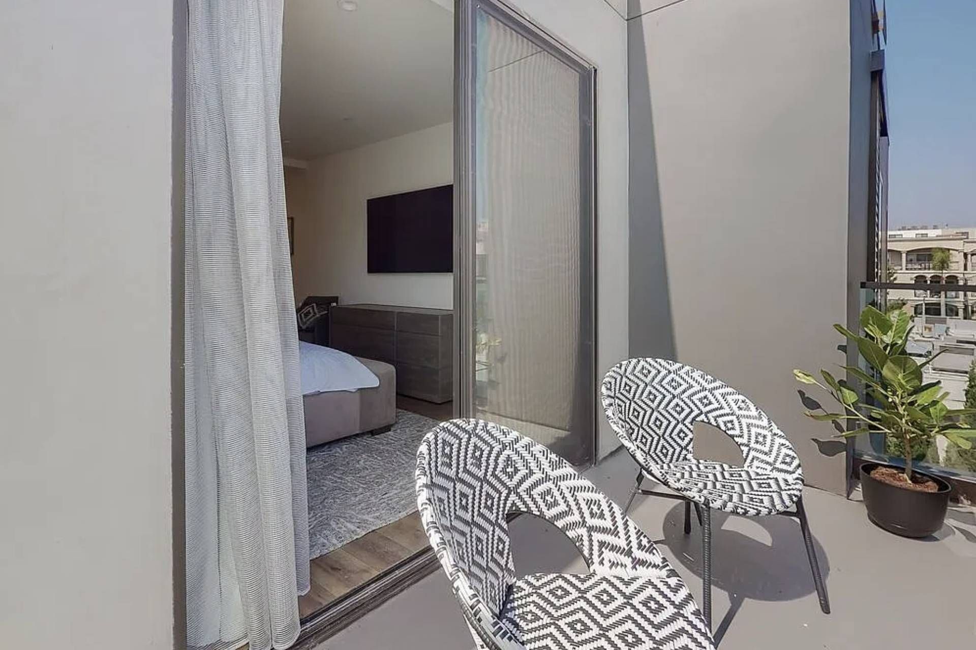 A balcony with a bed, a TV, and two patterned chairs.