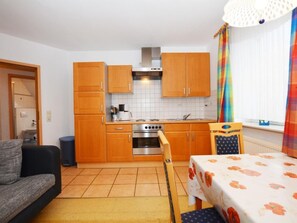 A compact kitchen with wooden cabinets, a built-in oven, and a dining area with a table. - Wunderschönes Appartement in Büsum mit Grill by Interhome (Büsum)