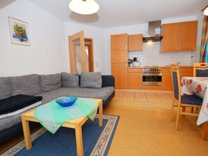 A compact living space with a sofa, a small dining table, a kitchen area with wooden cabinets and a stove, and a door leading to another room. - Wunderschönes Appartement in Büsum mit Grill by Interhome (Büsum)