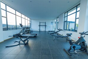 A gym with various exercise equipment, large windows, and a view of the outdoors. - Serene One Bedroom Apartment at the heart of Westlands, Kenya (Nairobi)
