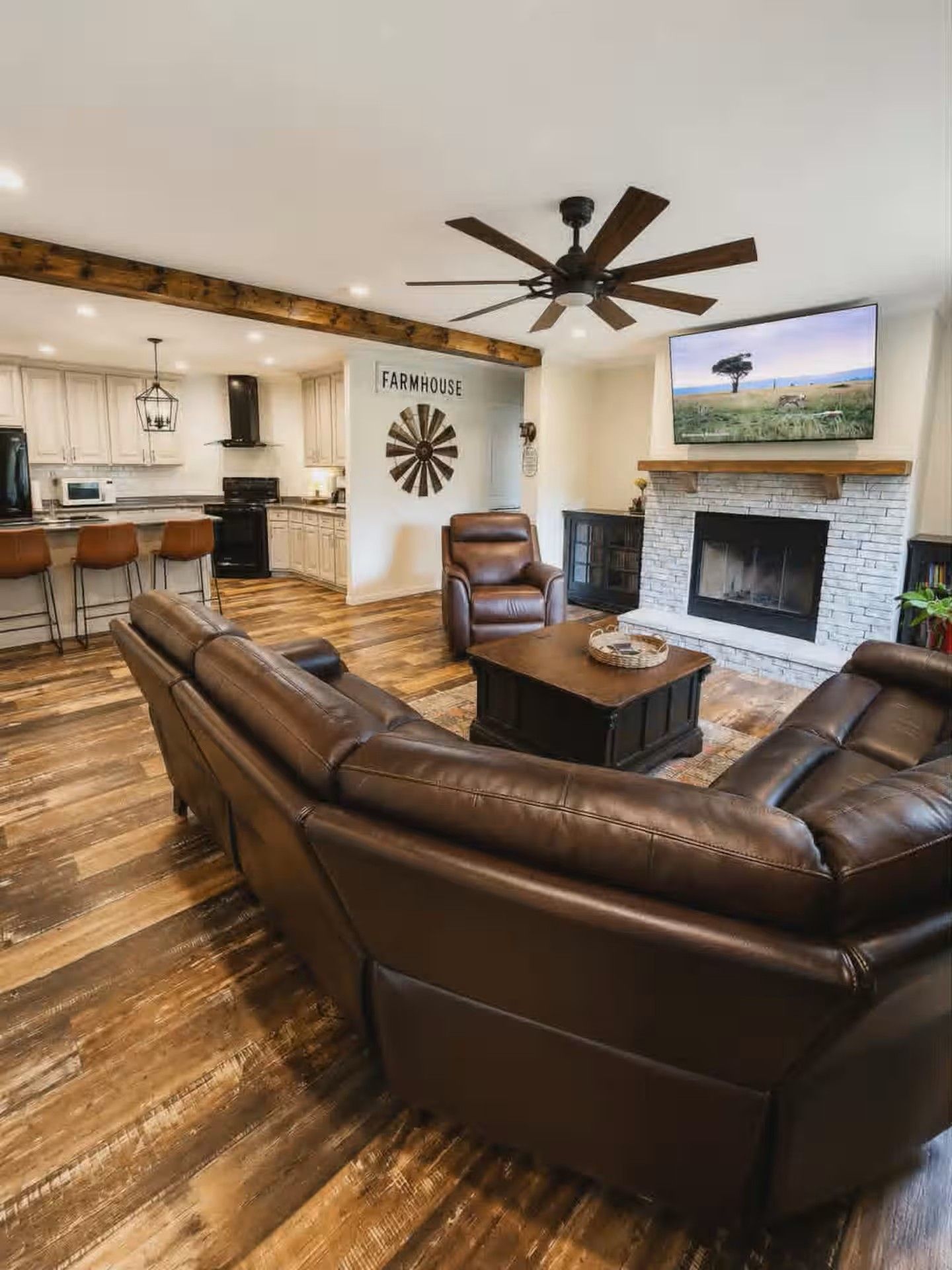 A living room with a sectional sofa, a fireplace, and a television mounted above it.