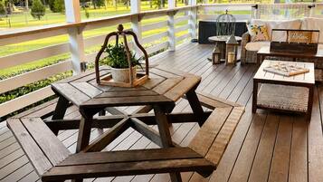 A covered outdoor area with wooden picnic tables and benches, a seating area with cushions, and a view of a green landscape.