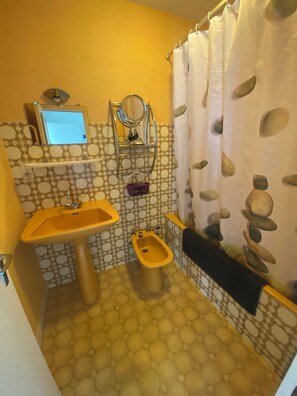 A bathroom with a yellow sink, a bidet, a mirror, and a shower curtain with a stone pattern. - Royan - One-bedroom apartment for 4 people with a balcony and private parking, near the beaches and downtown (Royan)