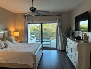 A bedroom with a bed, a nightstand, a dresser, a ceiling fan, a TV, and a balcony with chairs. - 3BR Gulf & River Views | 2 Pools | Beach Access (Pensacola)