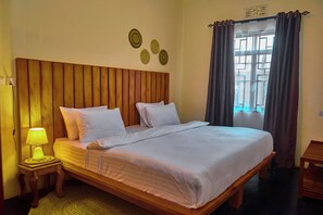 A bed with a wooden headboard, white bedding, and a bedside lamp.