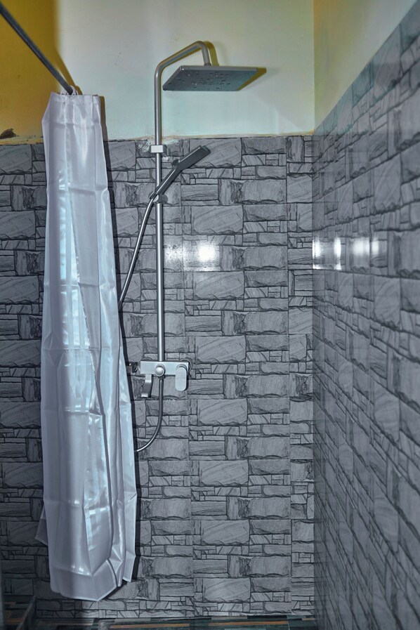 A shower area with a curtain, a handheld showerhead, and a wall with a stone-like pattern.