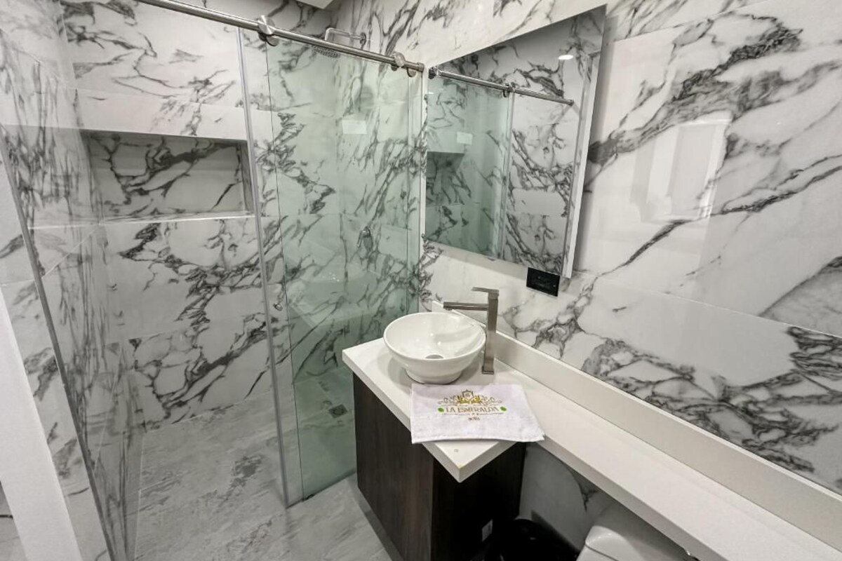 A bathroom with a glass shower enclosure, a marble-tiled wall, a white sink with a bowl, and a towel on the counter.