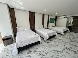 Una habitación de hotel con tres camas, piso de mármol y un adorno verde en la pared.