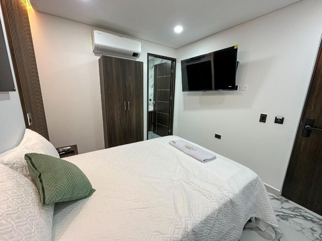 Un dormitorio con una cama, un televisor montado en la pared y un equipo de aire acondicionado.