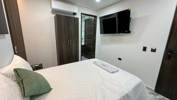 Un dormitorio con una cama, un televisor montado en la pared y un equipo de aire acondicionado.