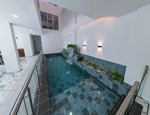 Piscina interior moderna con barrera de vidrio, paredes de azulejos e iluminación empotrada.