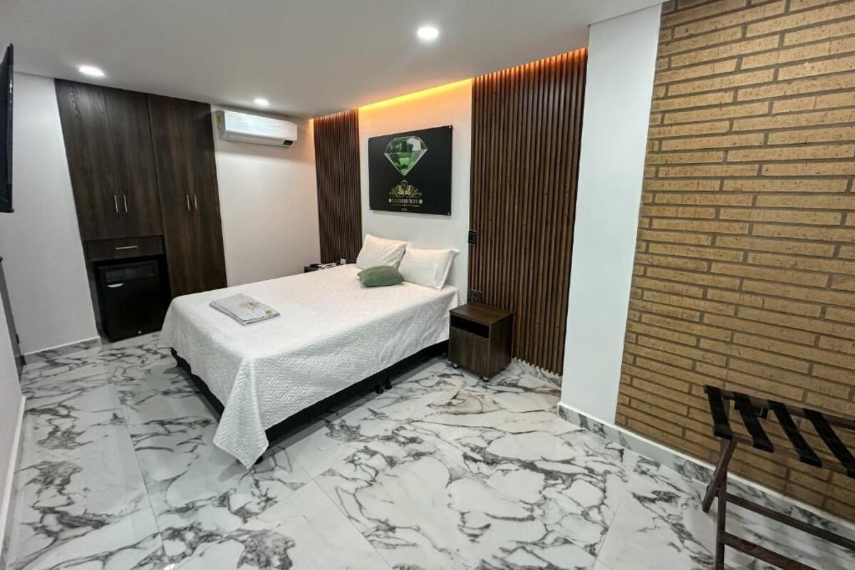 A bedroom with a bed, a nightstand, a wardrobe, and a brick accent wall.