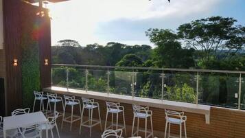 An outdoor seating area with tables and chairs, a glass railing, and a view of the surrounding forest.